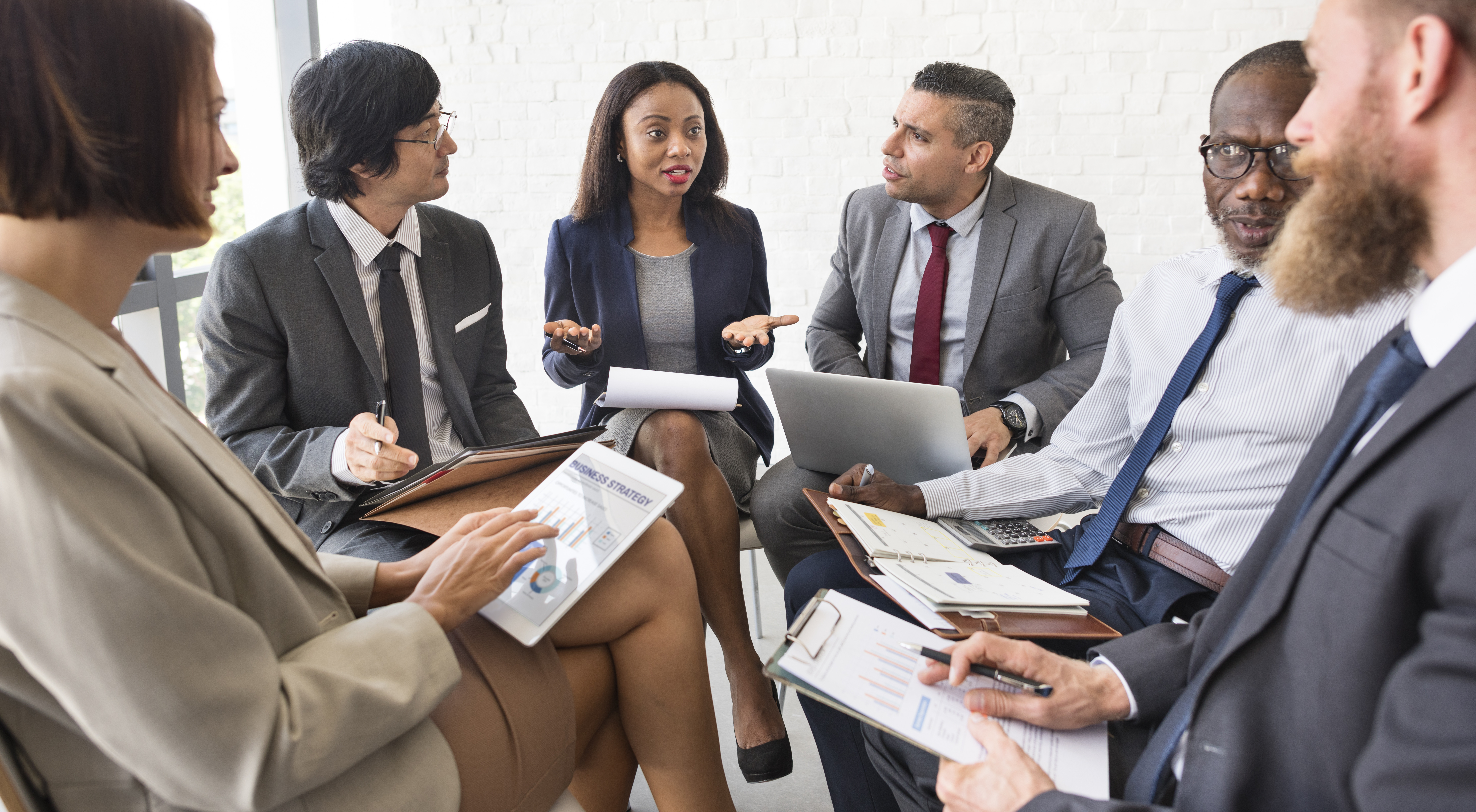 A group of executives sitting in a U-shape discussing what looks like work related business.